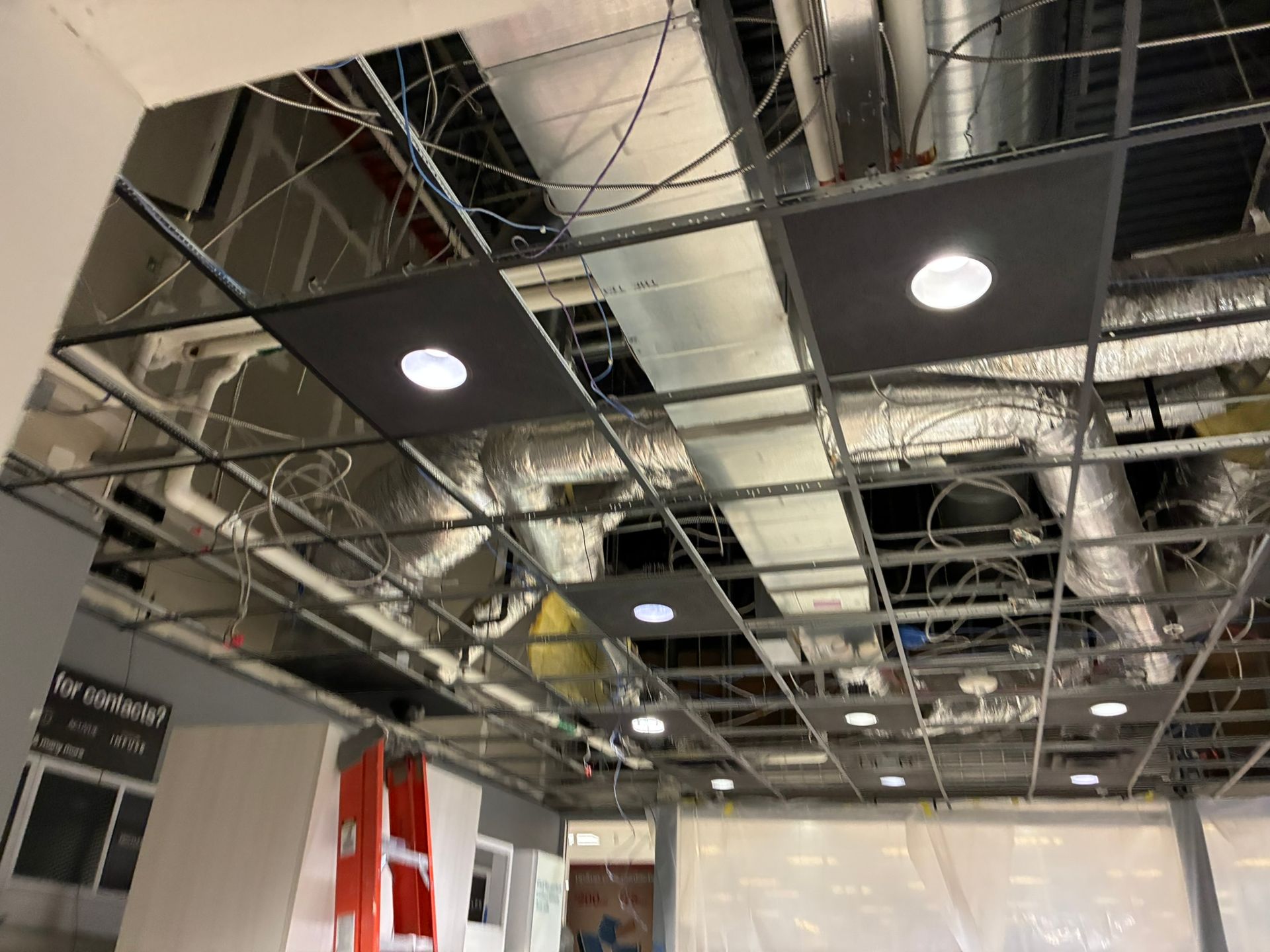 Ceiling under construction: metal grid, ductwork, wires, recessed lights, and gray acoustic panels.