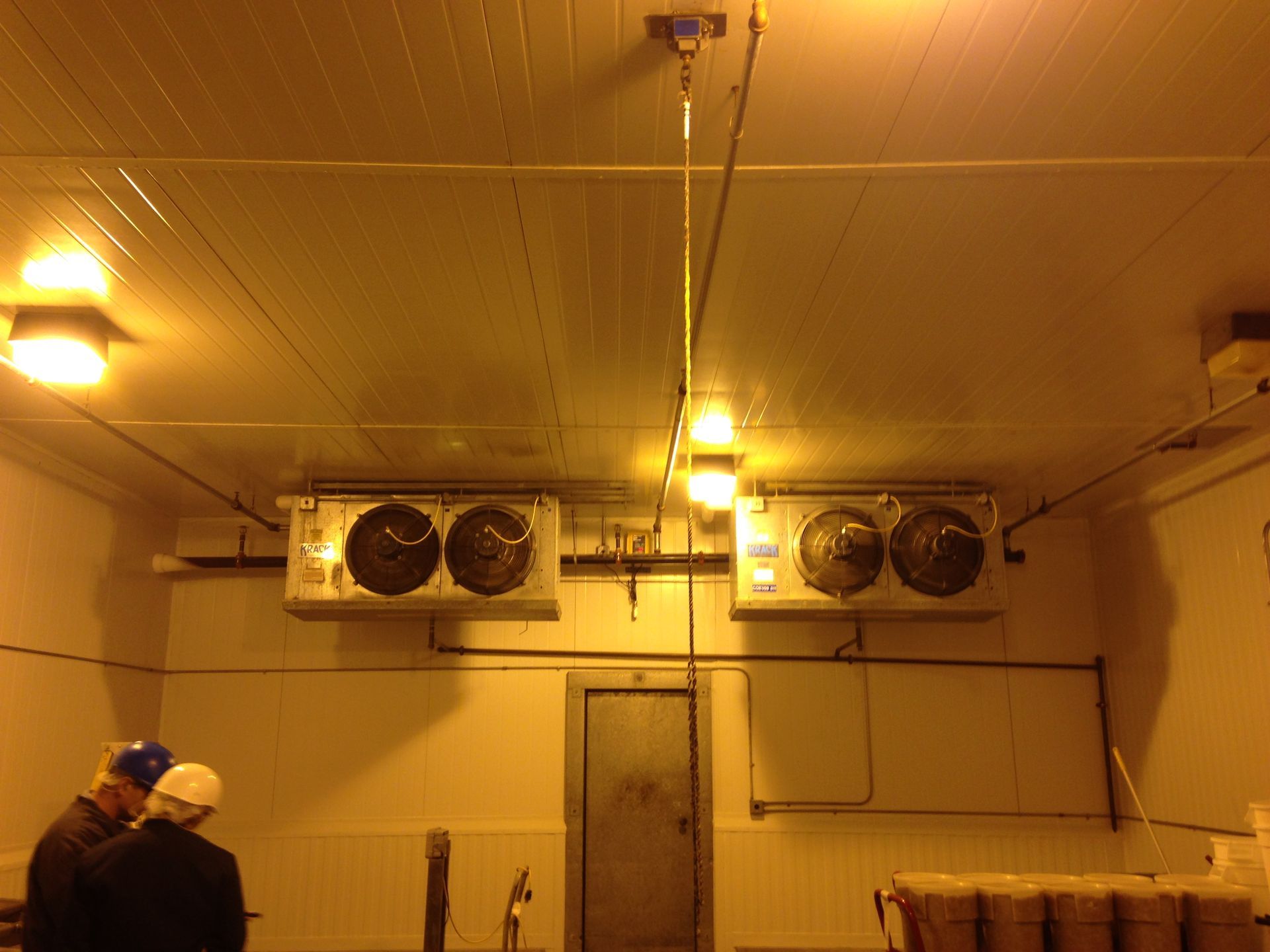 Interior of a cold storage room with two air conditioning units and two people standing at the bottom left.