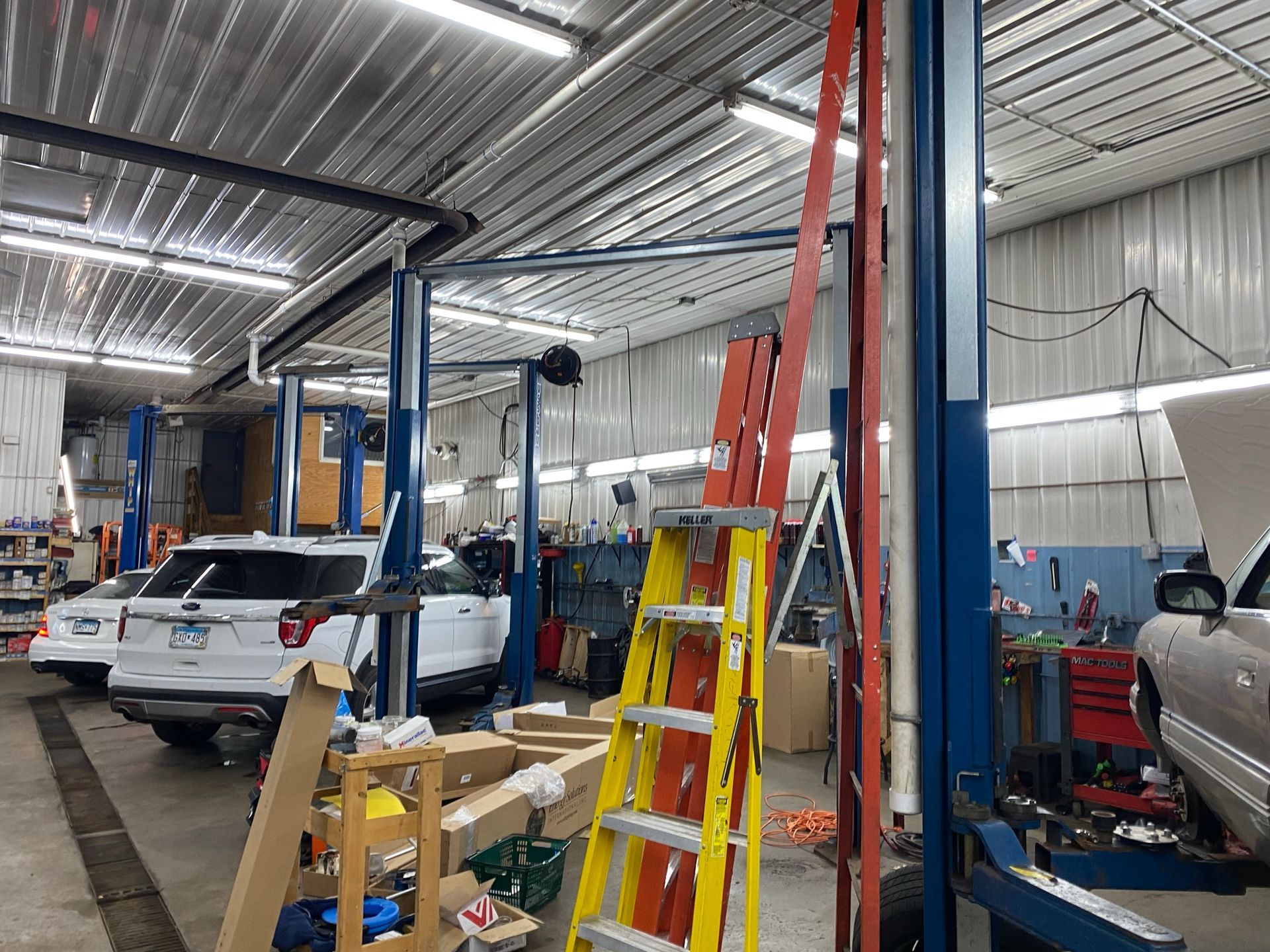 Auto repair shop interior with vehicle lifts, vehicles, and a ladder.