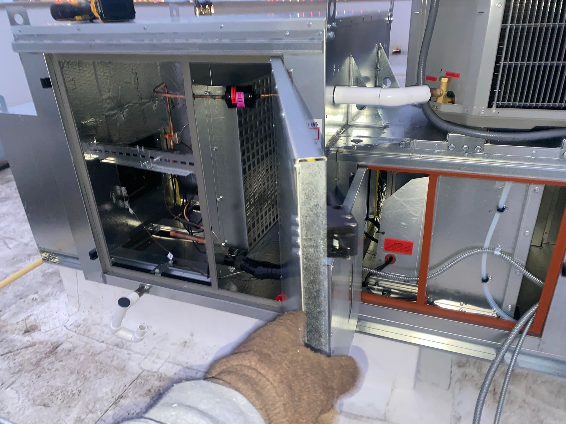 Person's gloved hand opens a panel on an HVAC unit, revealing interior components on a rooftop.