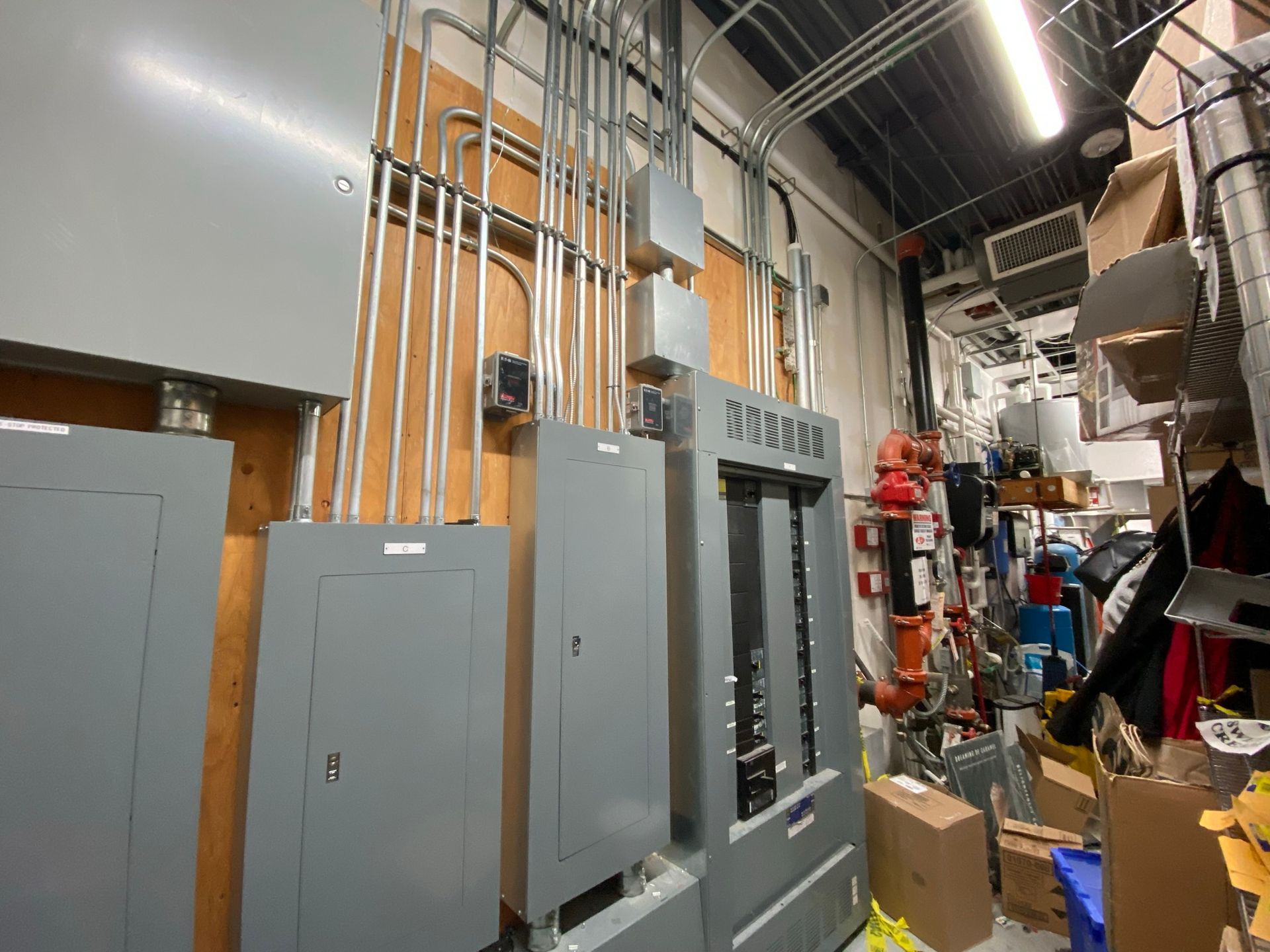 Electrical panels and conduits on a wall in a cluttered room.