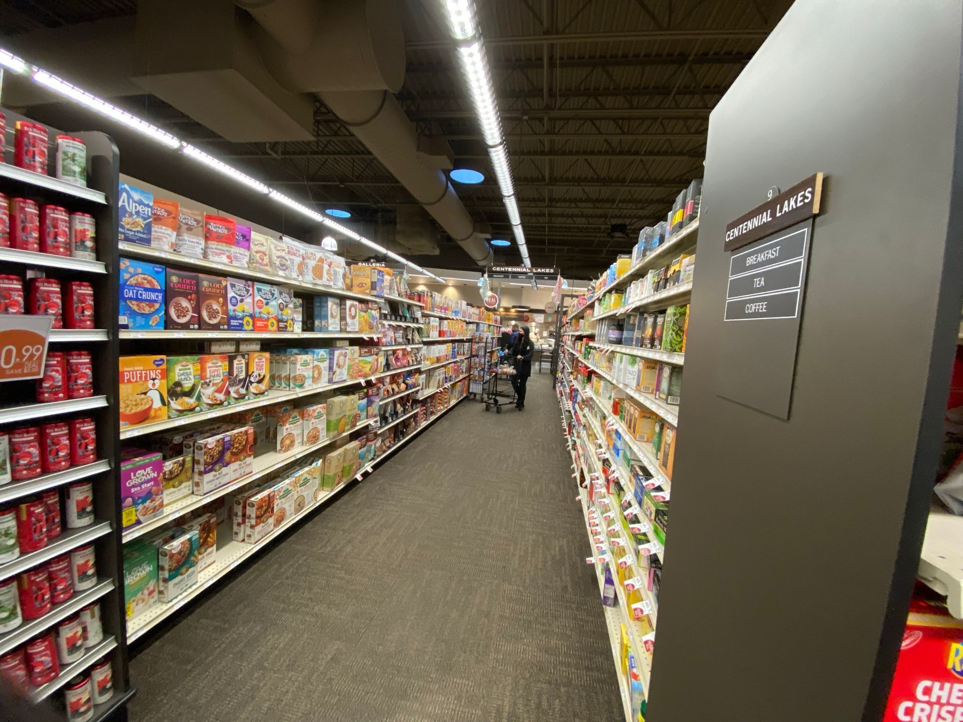 Grocery store aisle stocked with cereal boxes, with a person pushing a shopping cart.
