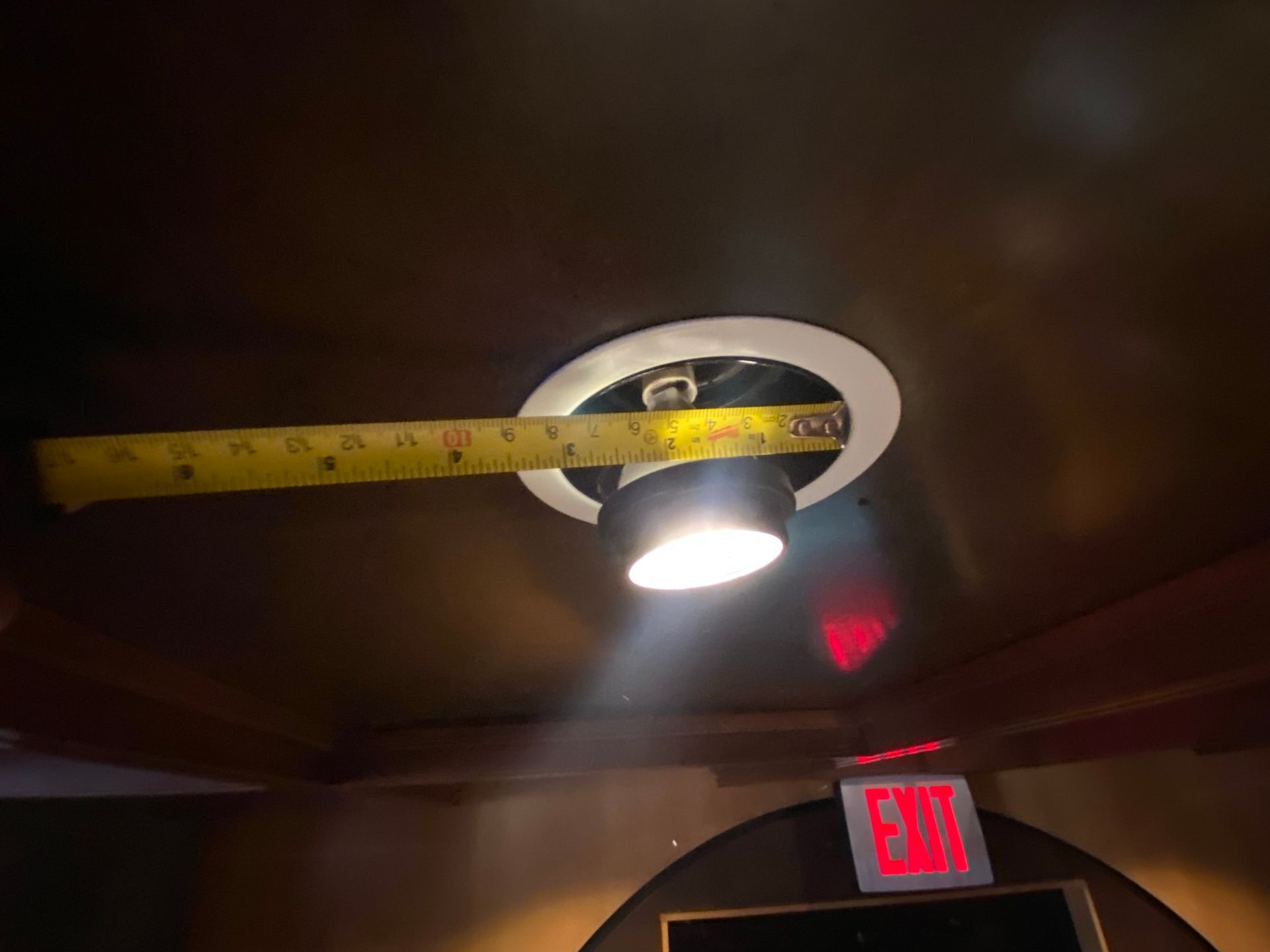 Ceiling light with tape measure. Light is on. An Exit sign is visible in the background.