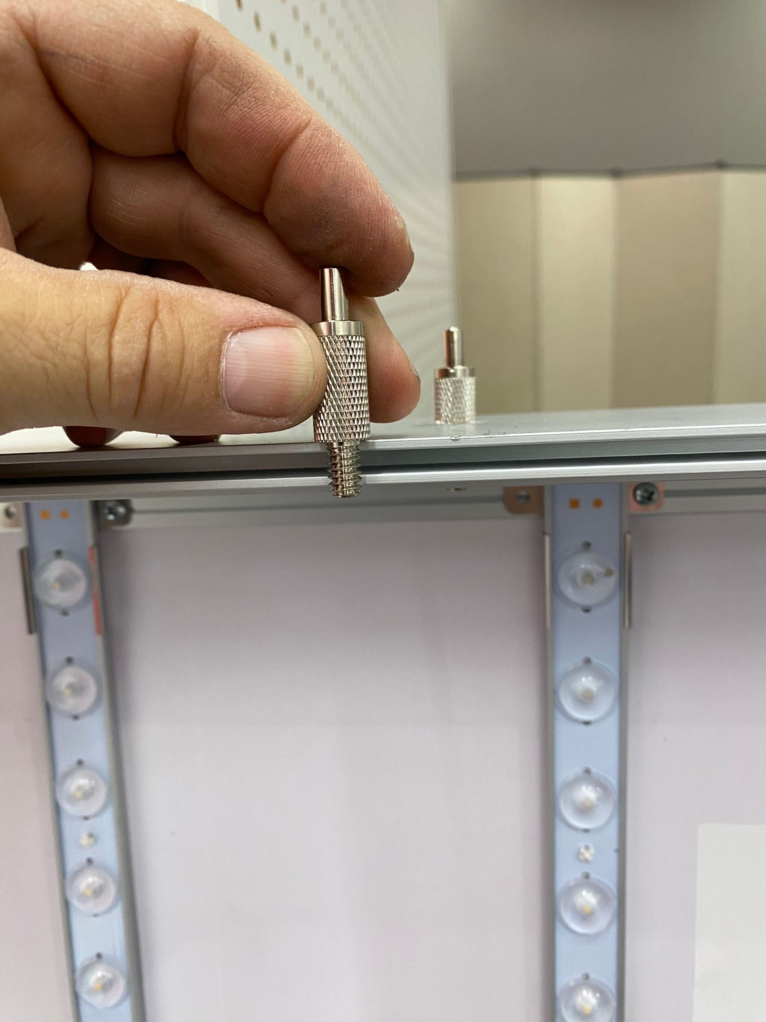 Hand holding silver connector, next to a similar one on a light panel with LEDs.