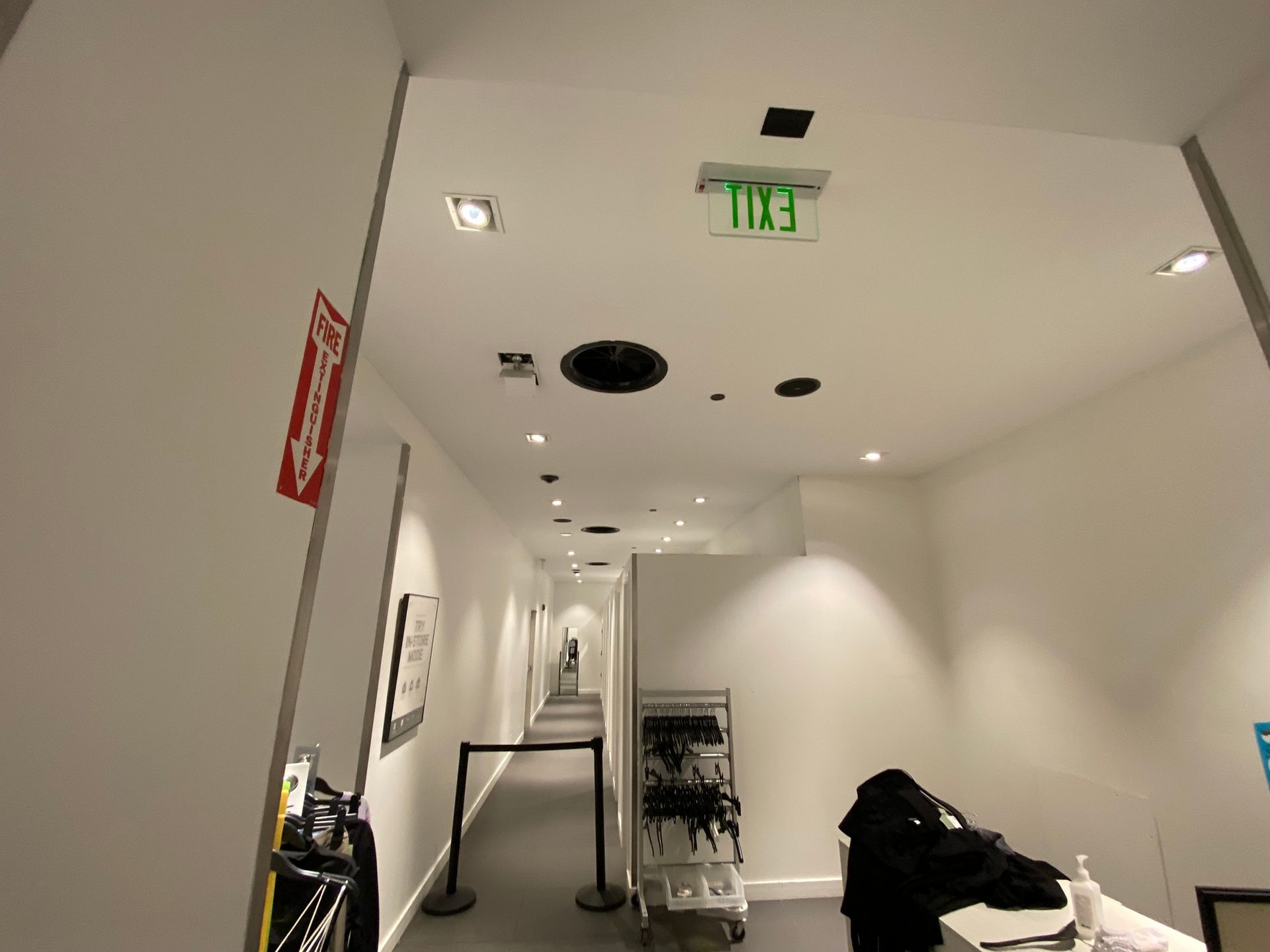 Long hallway with bright overhead lights, exit sign, and fire extinguisher.