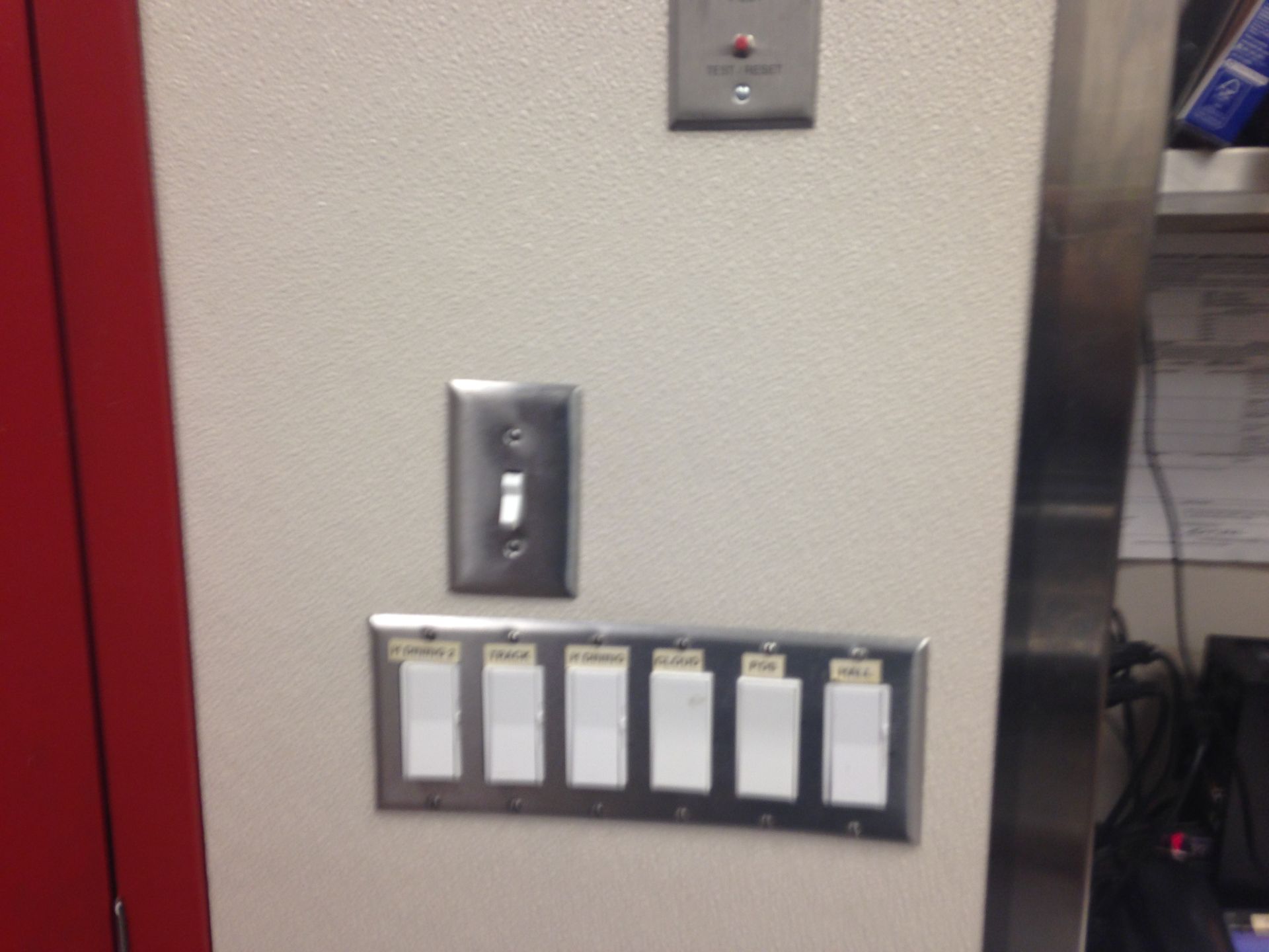 Panel with light switches. One toggle switch and a six-button panel with labels on a beige wall.
