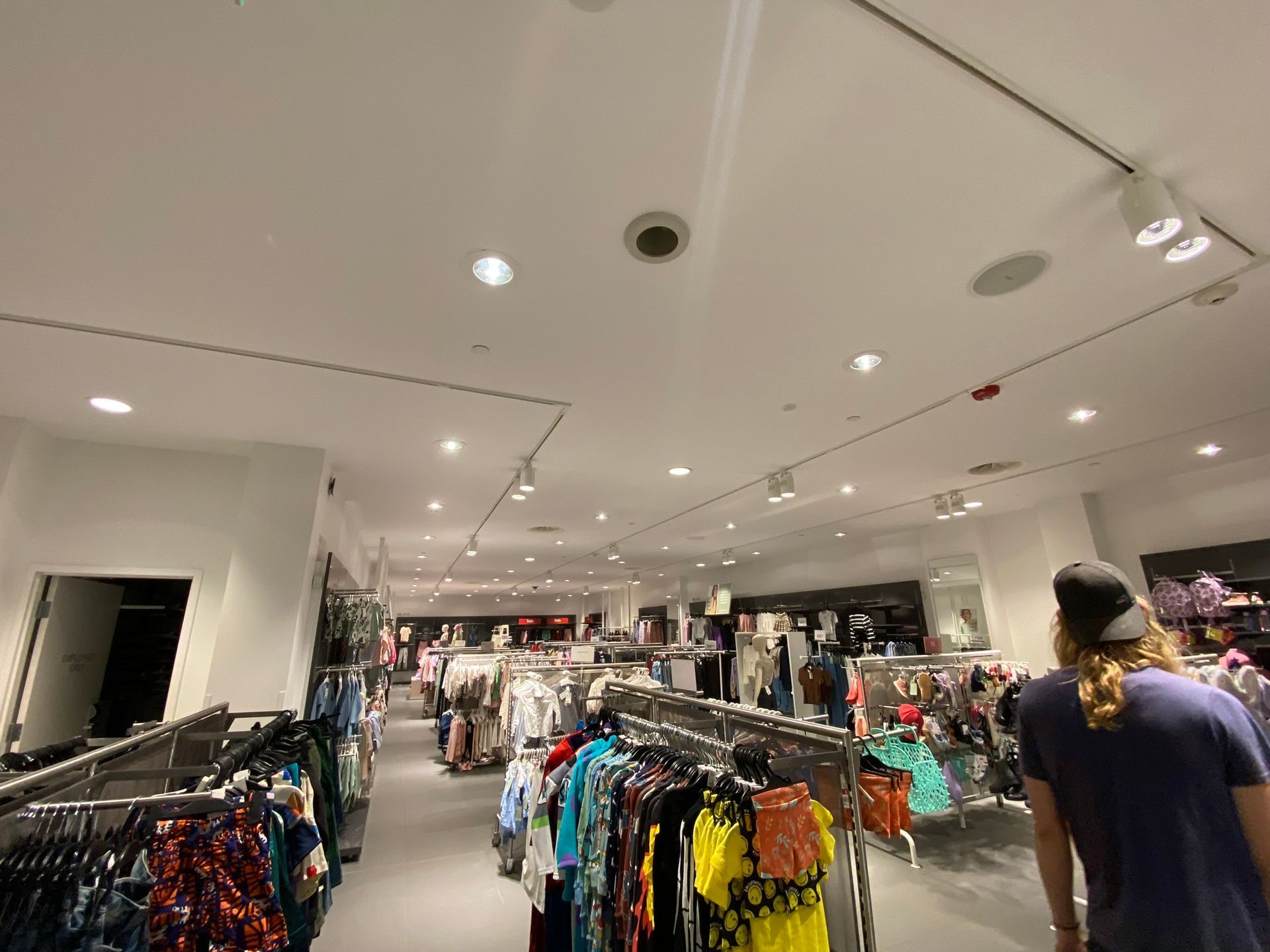 Clothes racks in a brightly lit clothing store. A person walks toward the back.