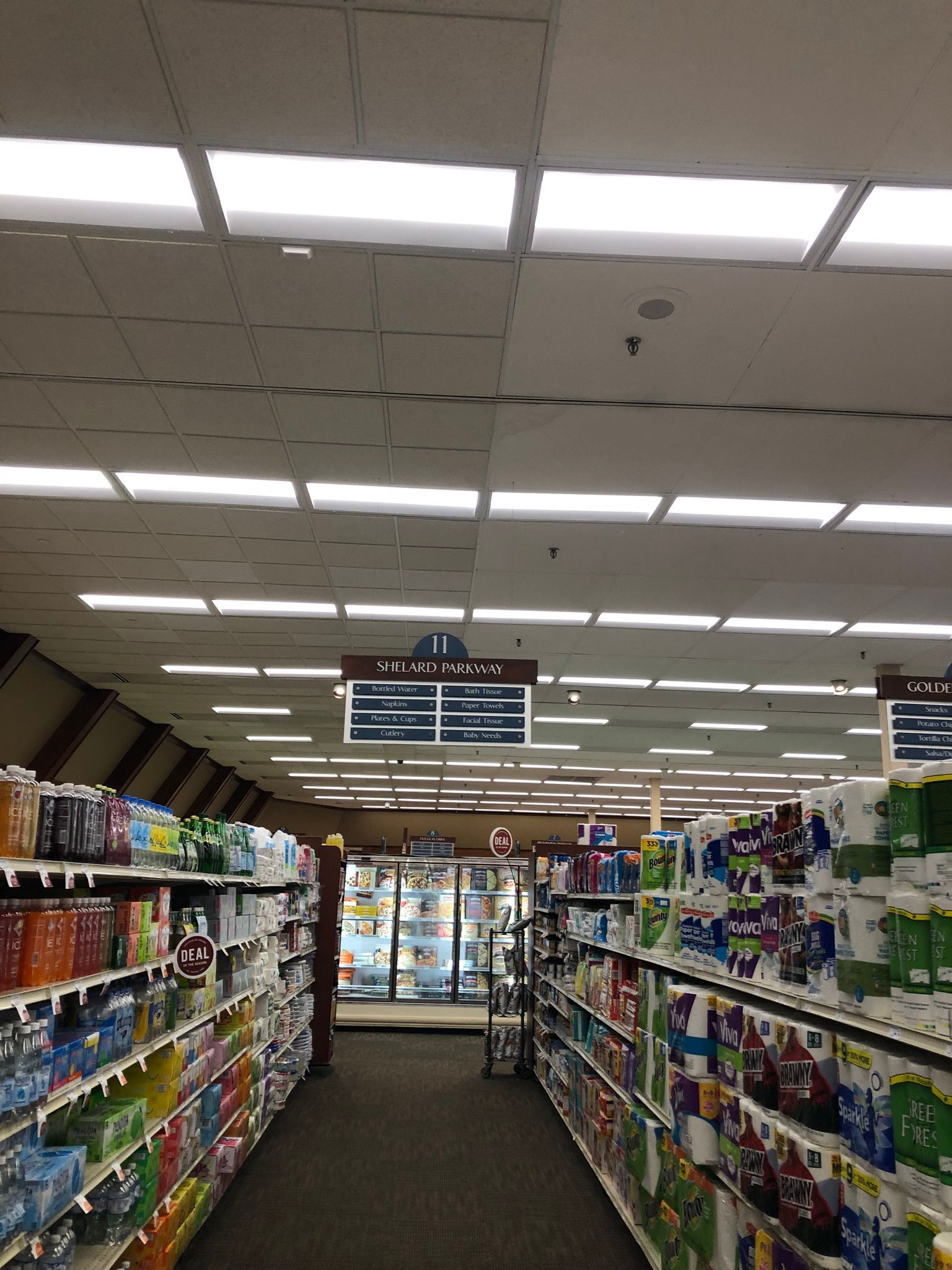 Grocery store aisle with shelves of products under bright fluorescent lights.