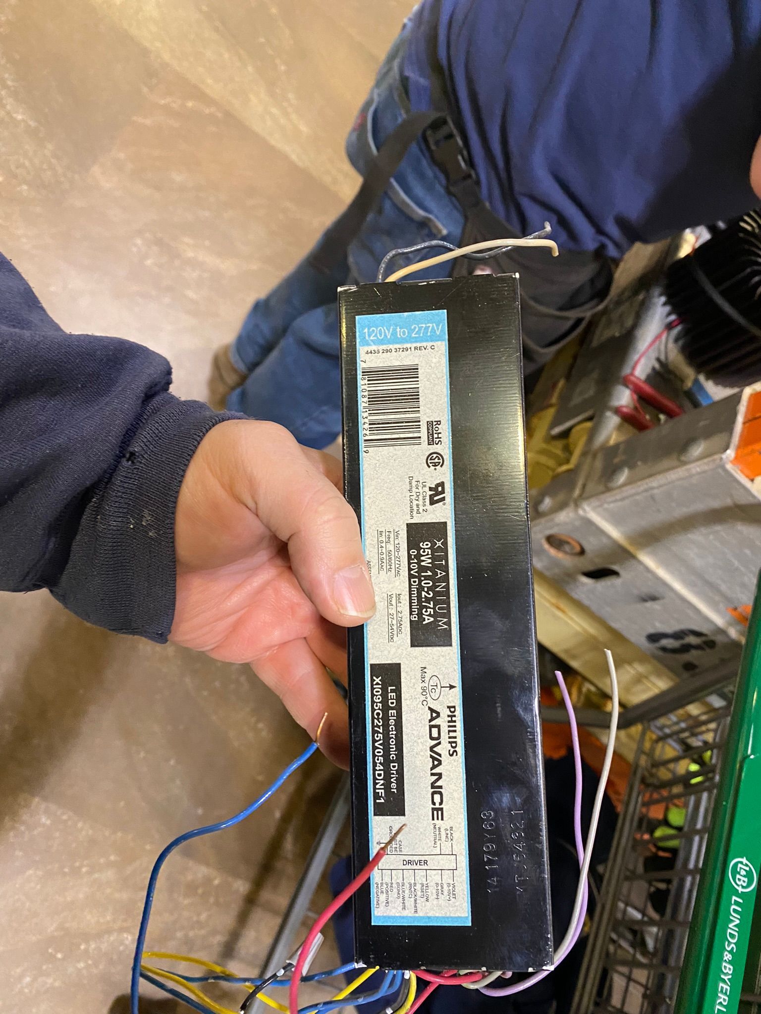 Person holding a black fluorescent light ballast with colored wires.