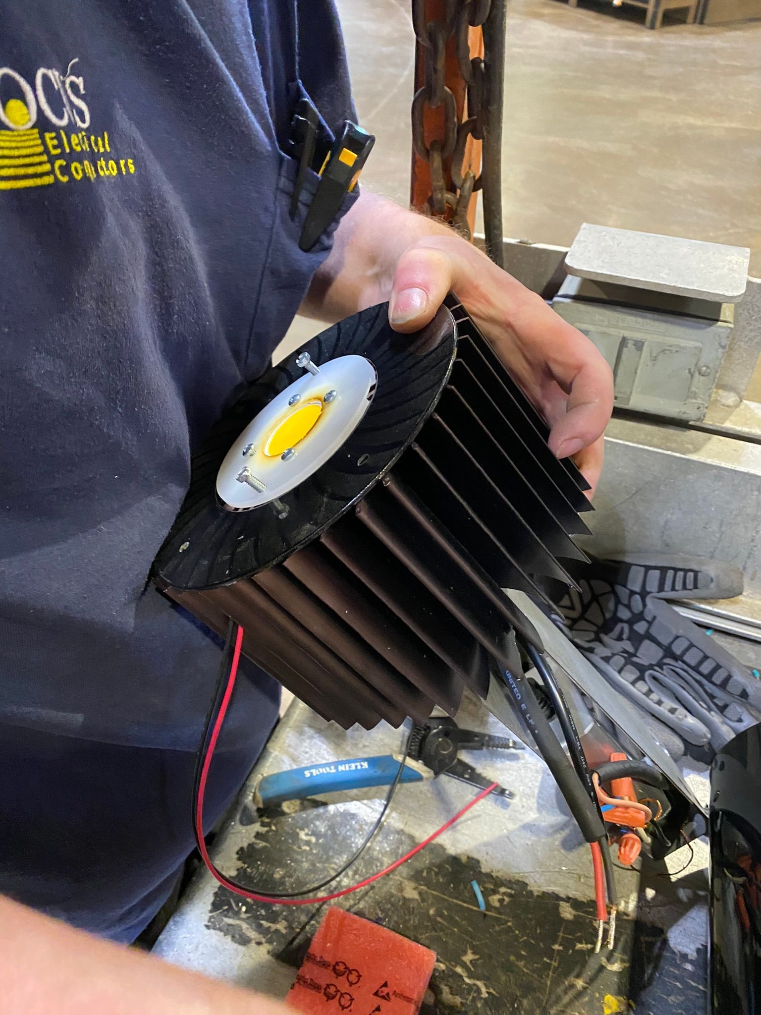 Person holding a black LED flood light with cooling fins, red and black wires visible.