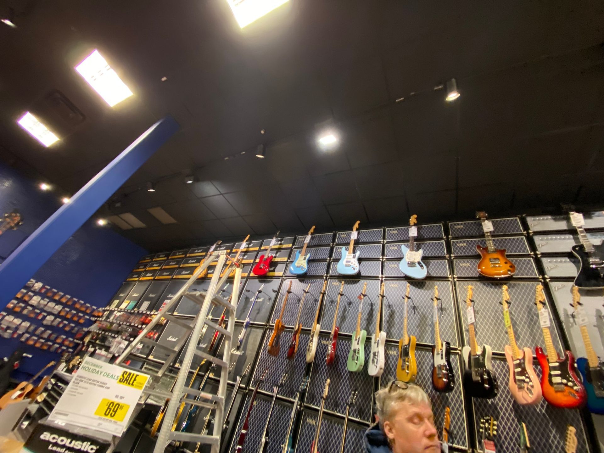 A guitar store with guitars on display. A man stands below the guitars looking up.