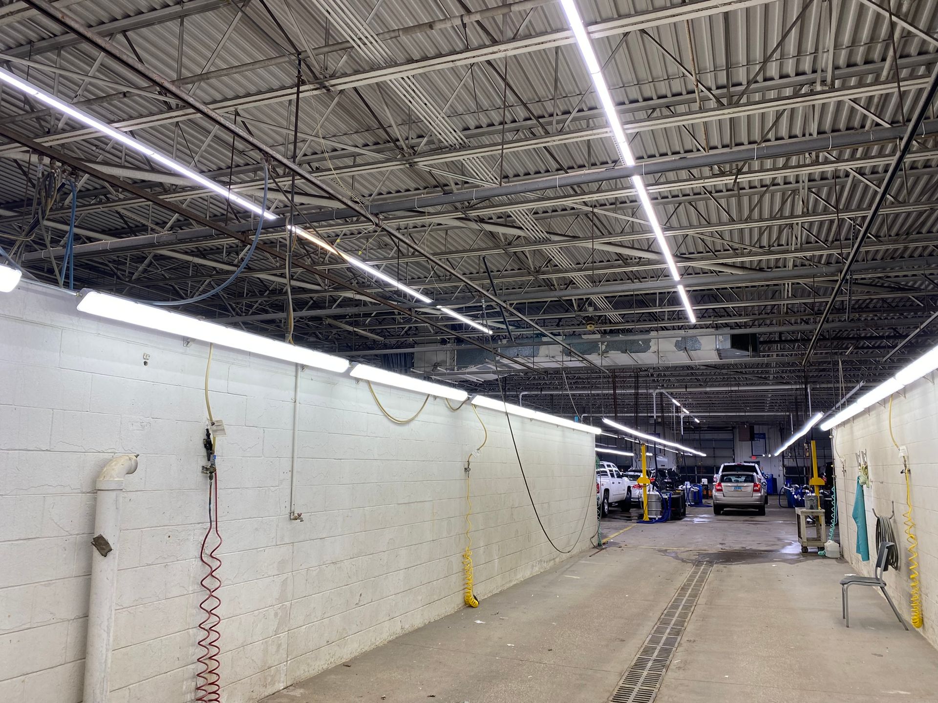Indoor car wash bay with high ceilings, bright lights, and white walls.