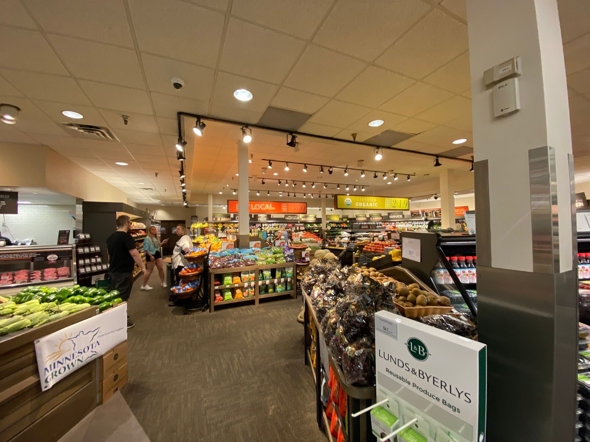 Interior view of a grocery store aisle filled with produce. People shop.
