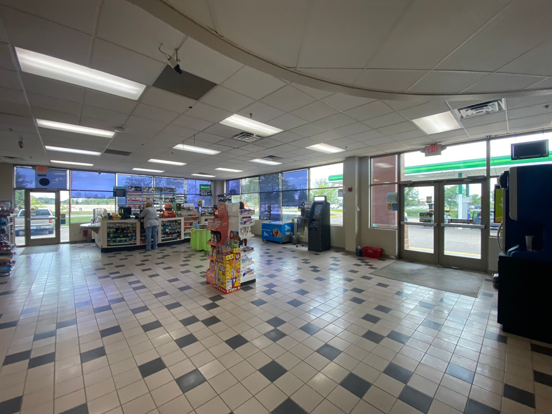 Interior of a convenience store with checkered floor, glass windows, and a BP gas pump visible outside.