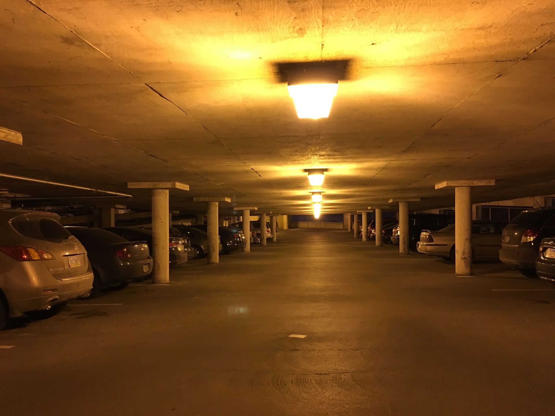 Underground parking garage with cars parked in rows, illuminated by overhead lights.