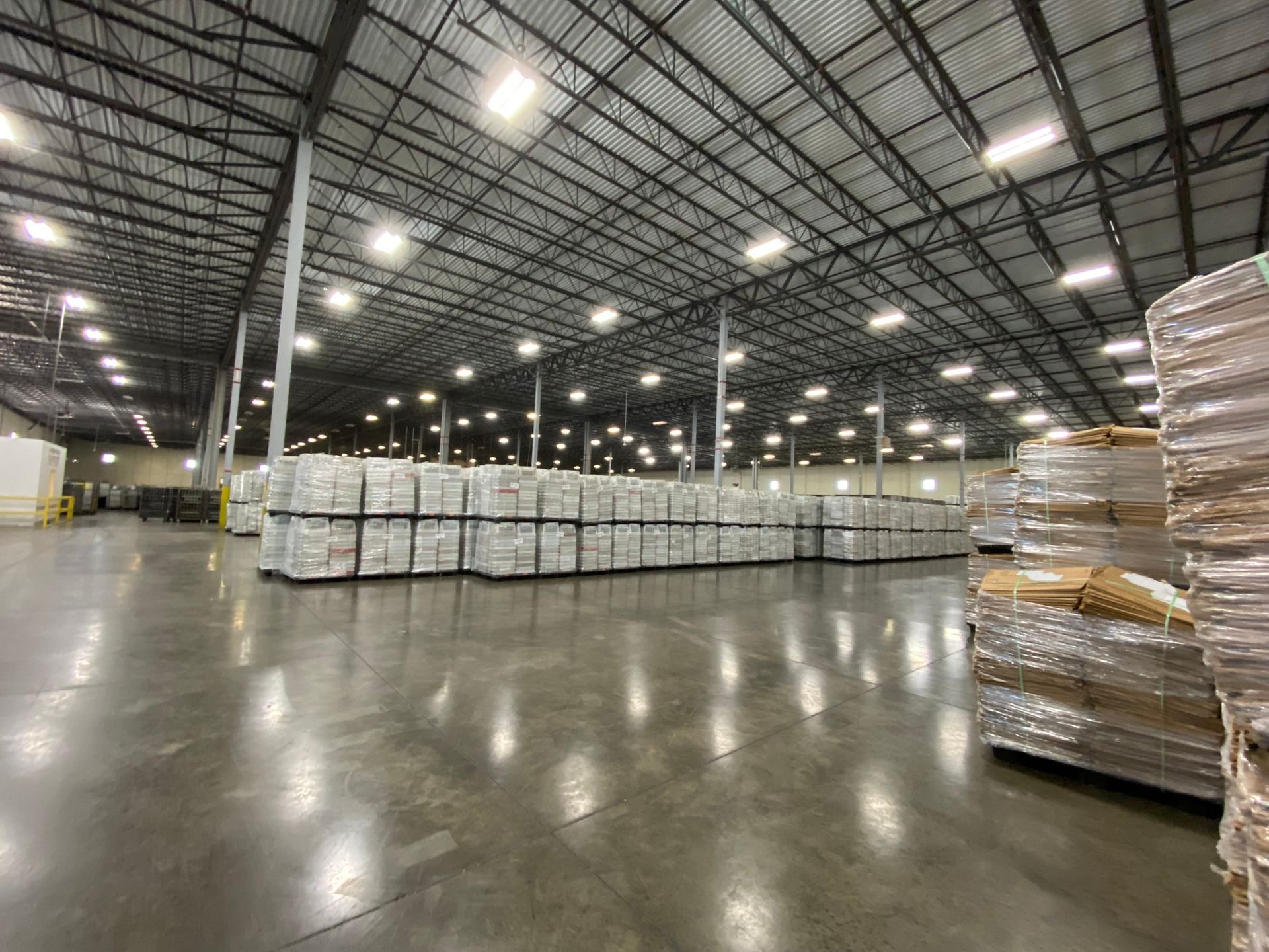 Large warehouse interior with rows of stacked pallets under bright lights.