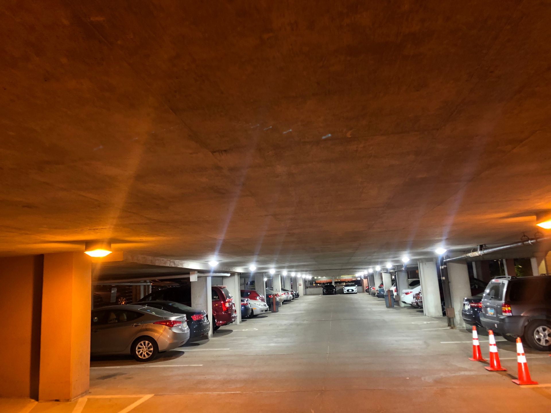 Underground parking garage with cars parked in rows, illuminated by overhead lights.