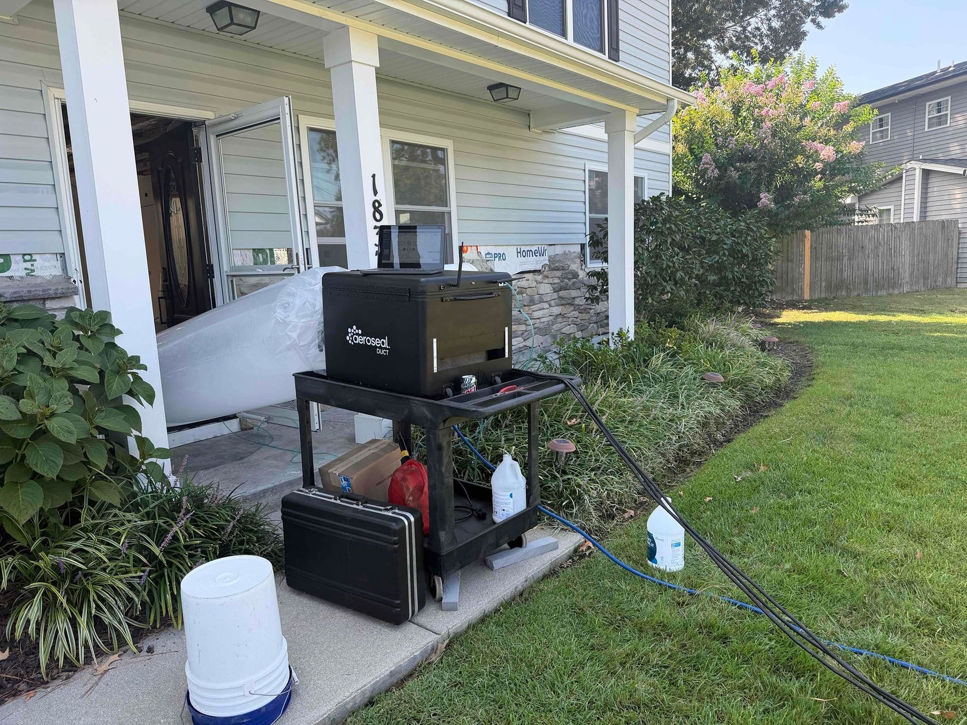 Black grill and accessories on a patio beside a white house, with lawn and garden beds nearby