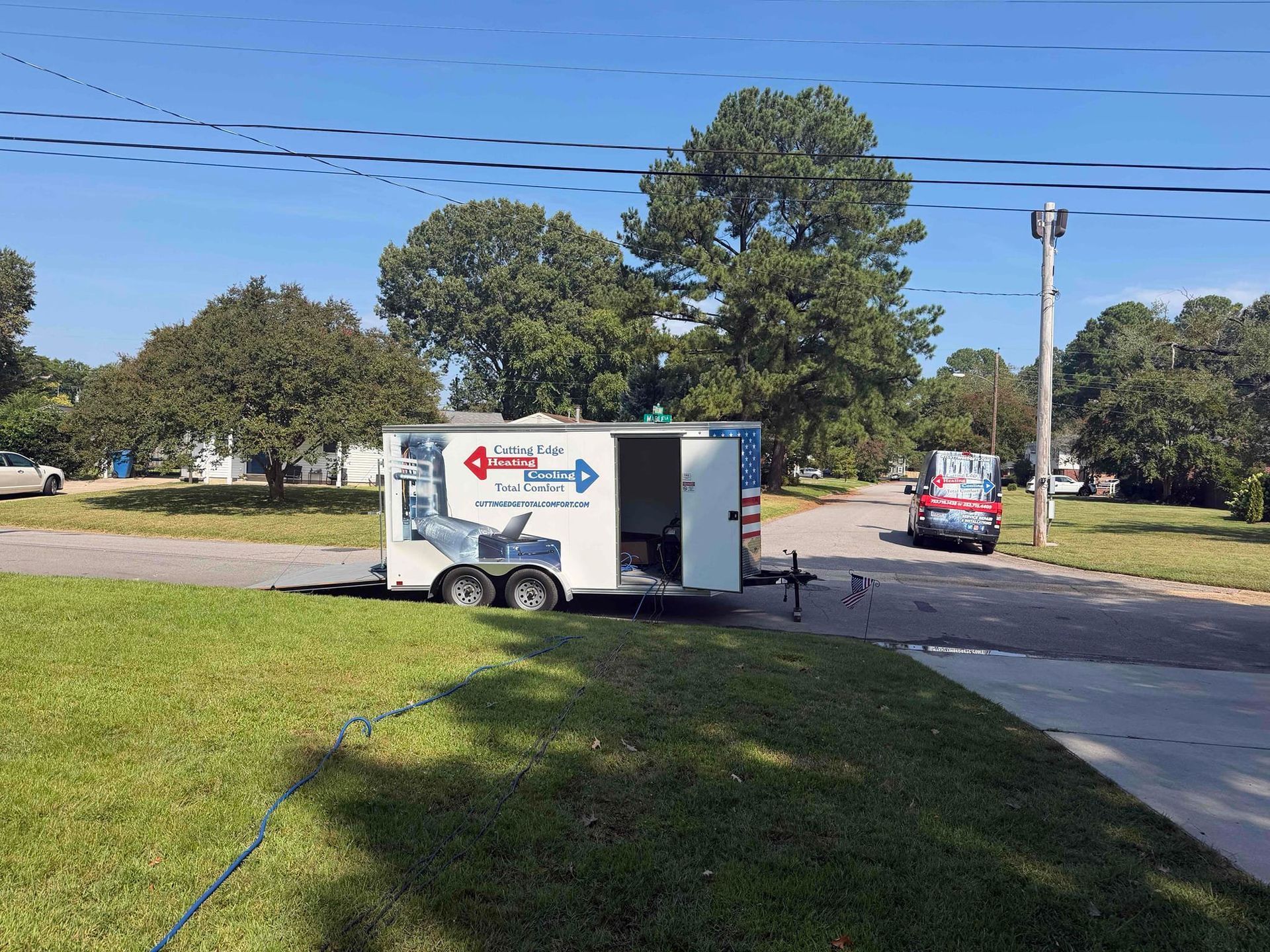 White enclosed trailer parked by a road with an open side door; red car in the background on a sunny day
