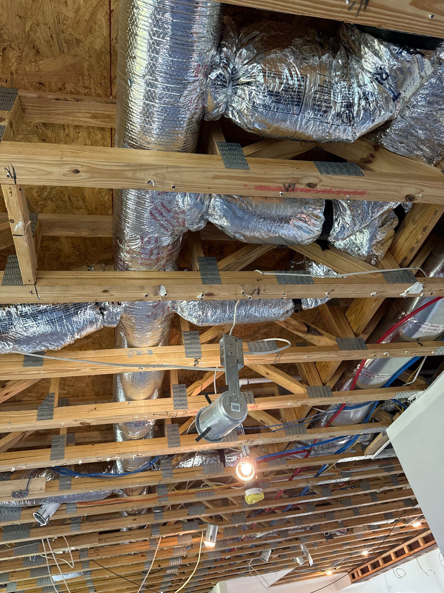 Exposed attic rafters with shiny silver HVAC ducts and a hanging light bulb during renovation