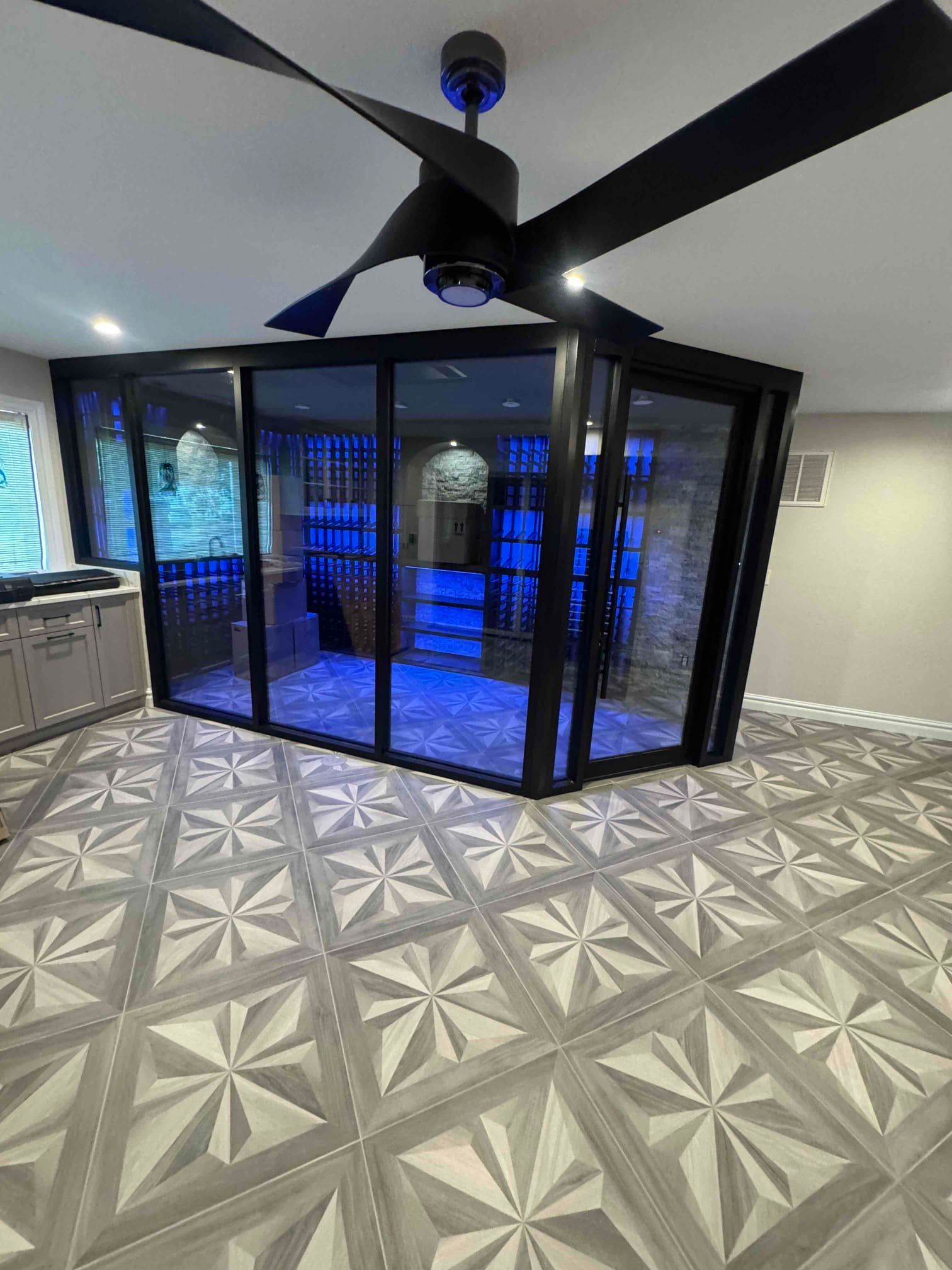 Indoor glass-enclosed sauna with blue lighting, ceiling fan, and geometric tile floor