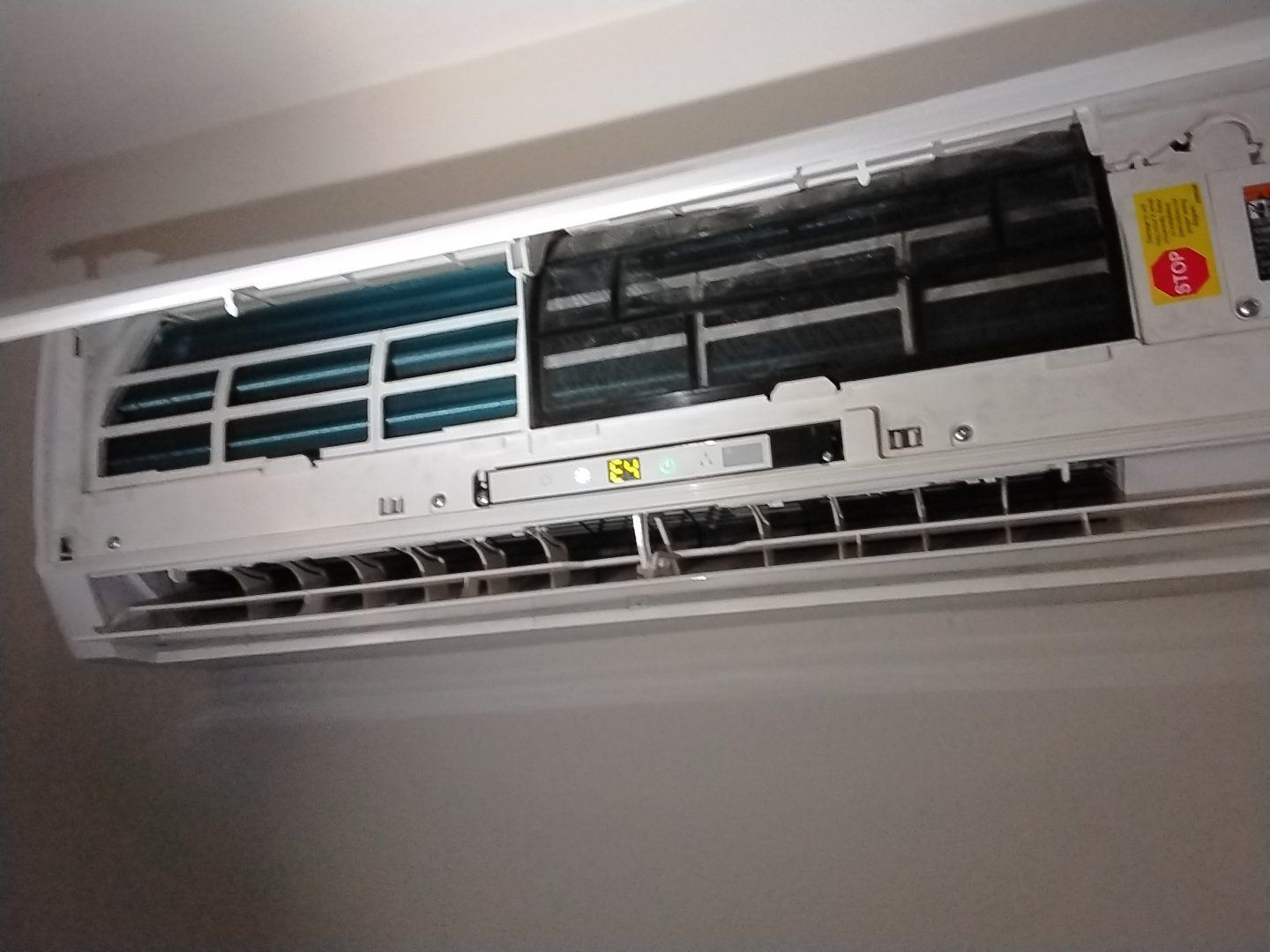 Wall-mounted air conditioner with front panel open, showing dark and light interior vents.