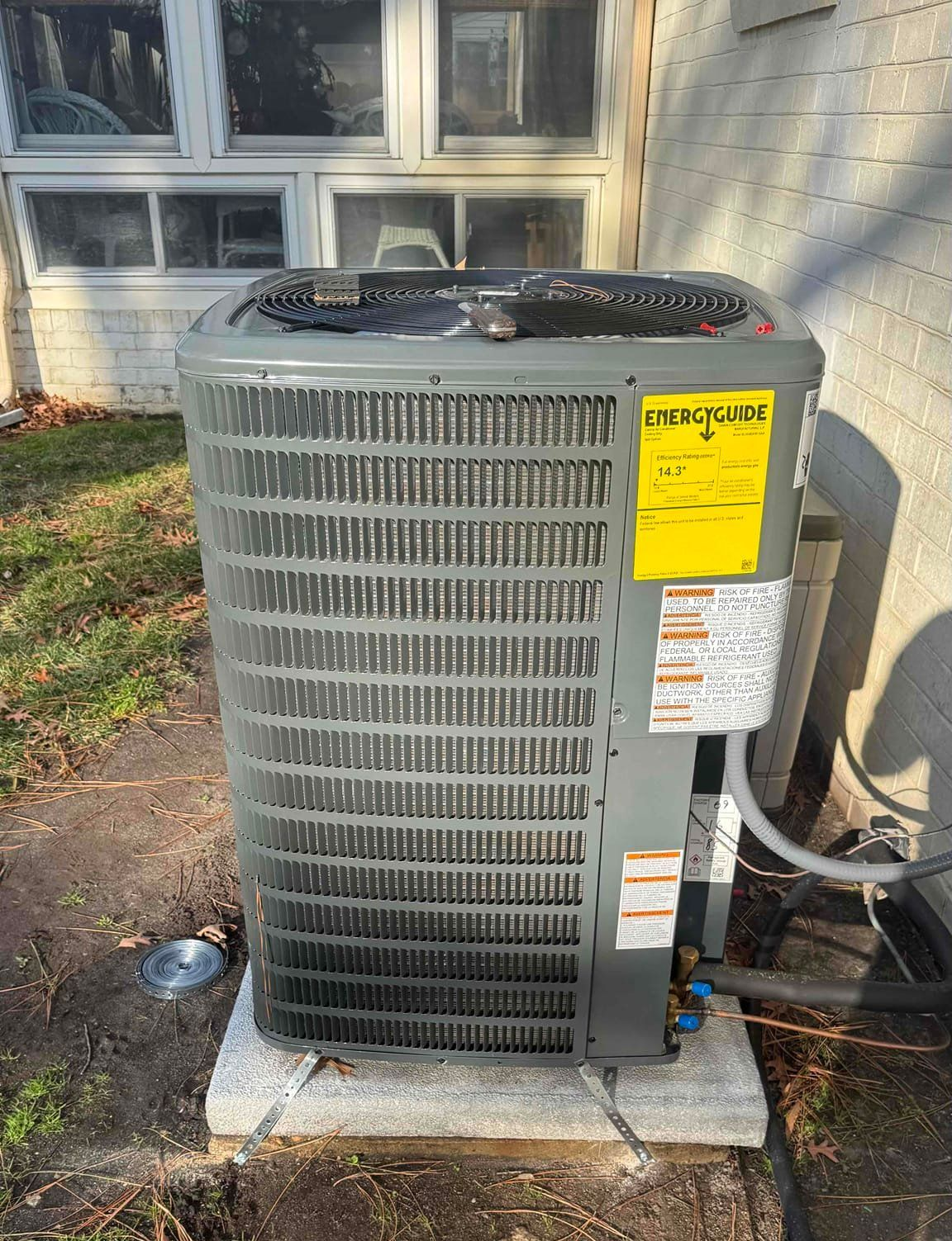 Outdoor central air conditioner unit beside a house, with warning labels on the front.