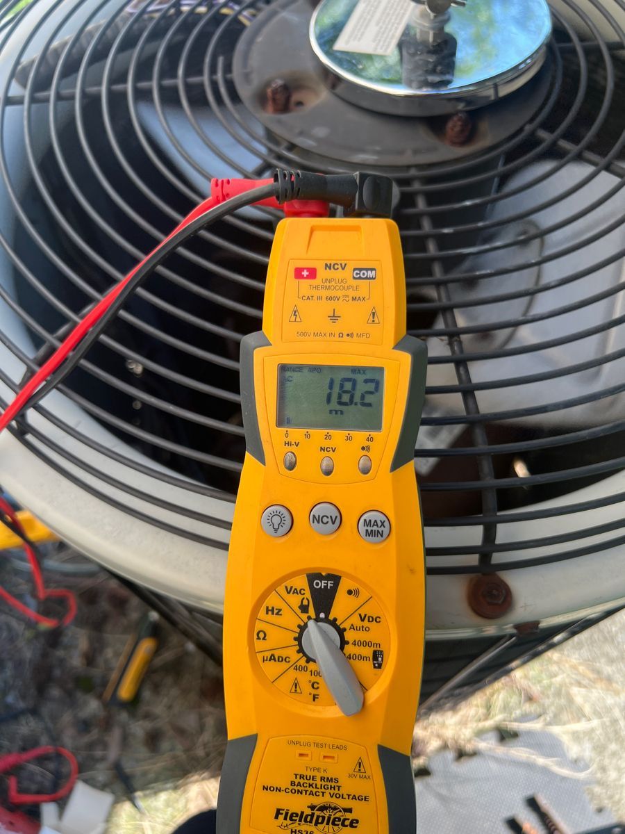 Yellow digital multimeter testing an outdoor AC unit fan motor with red probes.