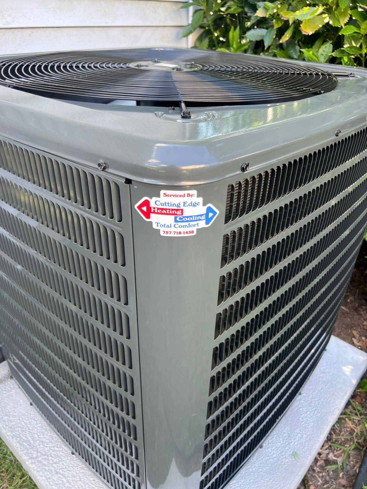 Outdoor air conditioner unit with black top fan grille and gray metal sides, shown close up.