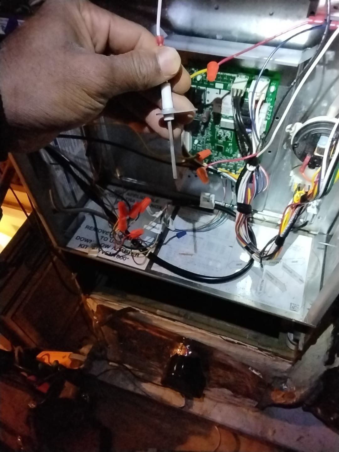 Hand holding a probe inside an open electrical control box with wires and circuit boards.
