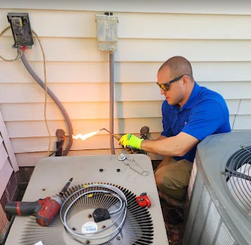 Technician repairing outdoor HVAC unit with a bright flame near wall-mounted equipment.