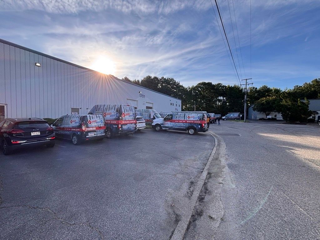 Parking lot beside a white warehouse with several cars and trucks under a sunny evening sky
