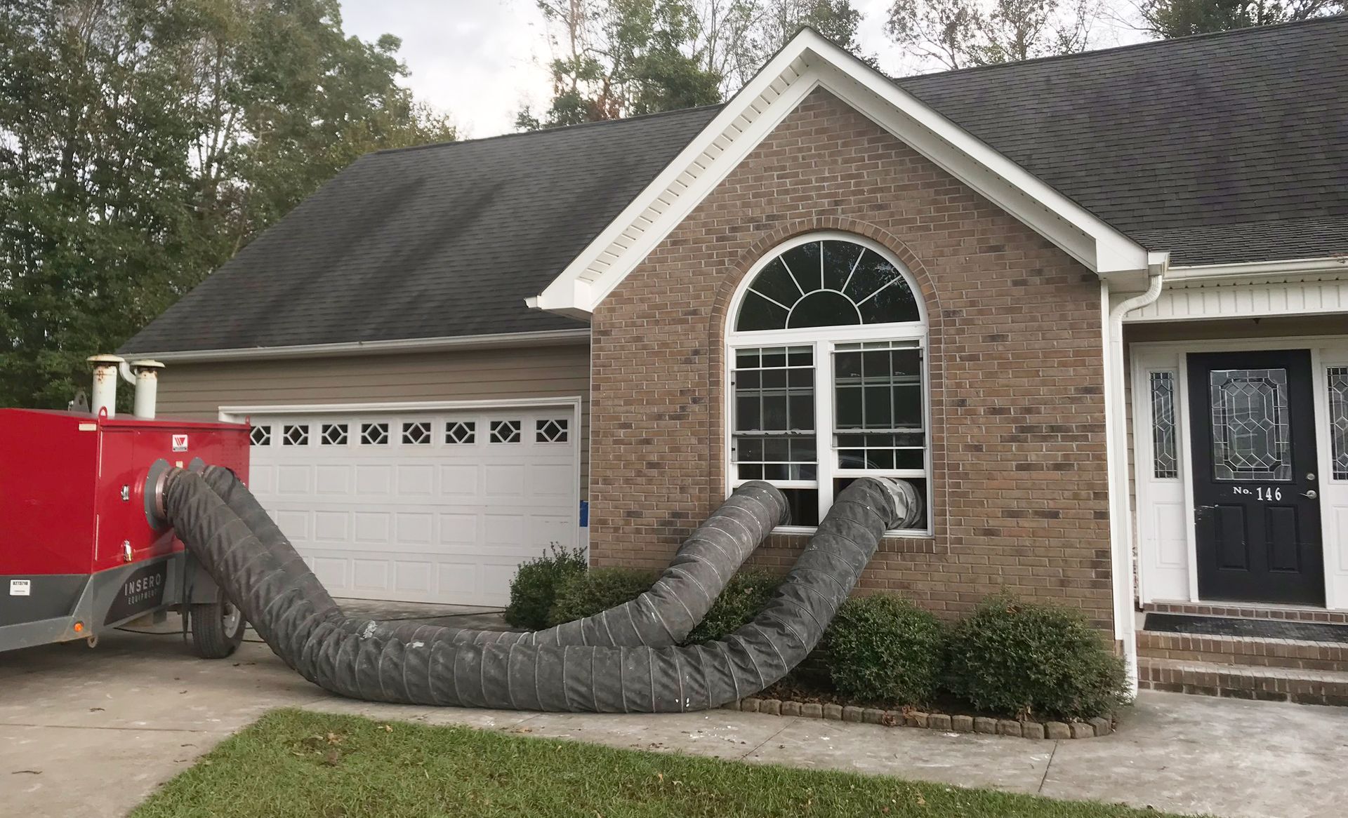 A red industrial machine with two hoses connected to a house window; for structural drying.