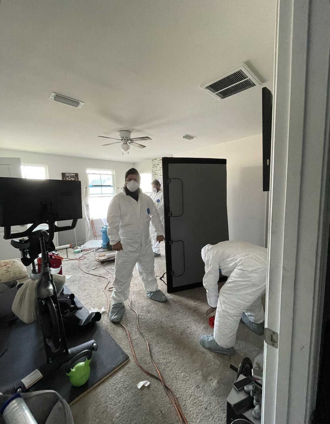 two men in protective suits are working in a living room