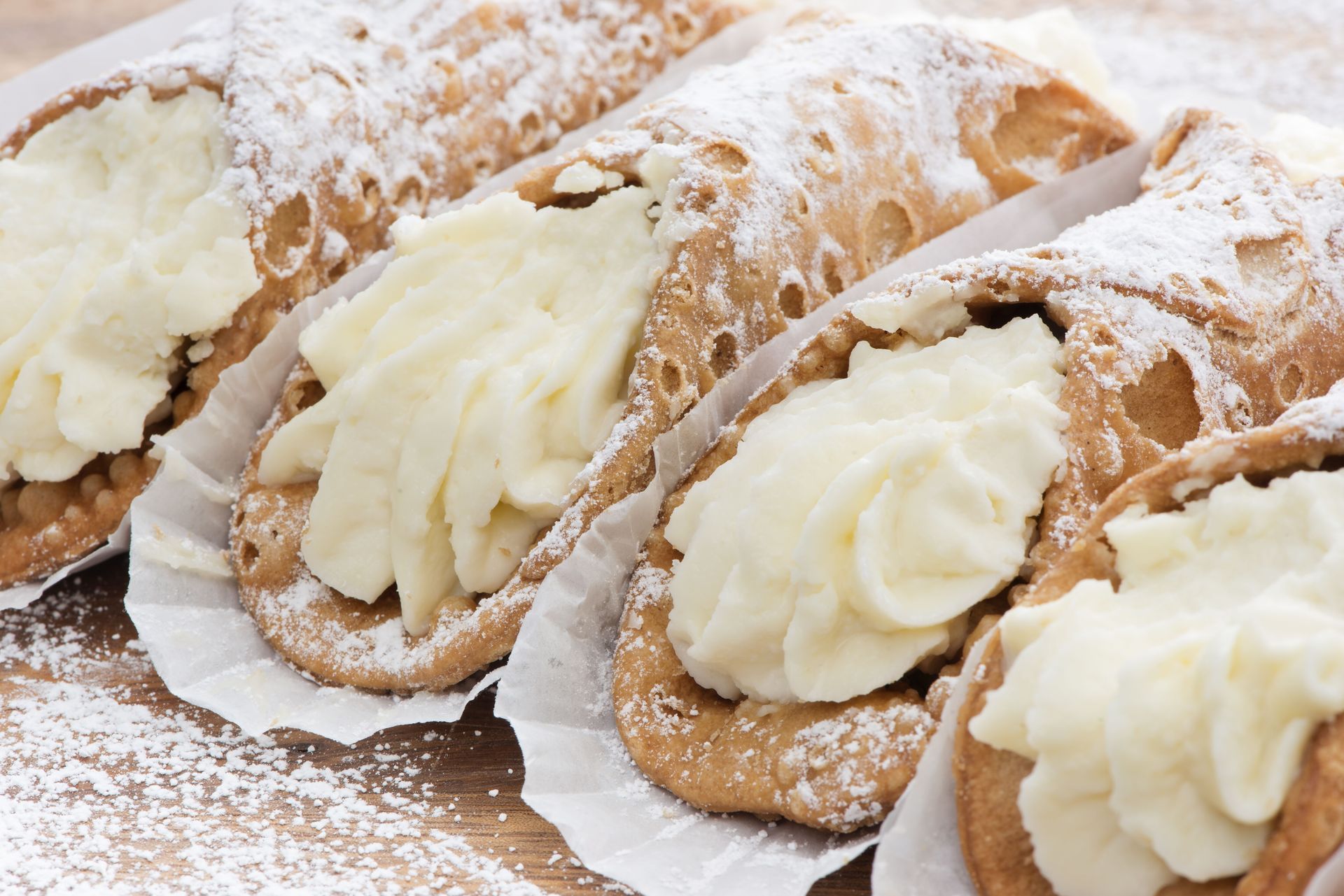 Four cannoli with whipped cream and powdered sugar on a wooden table.