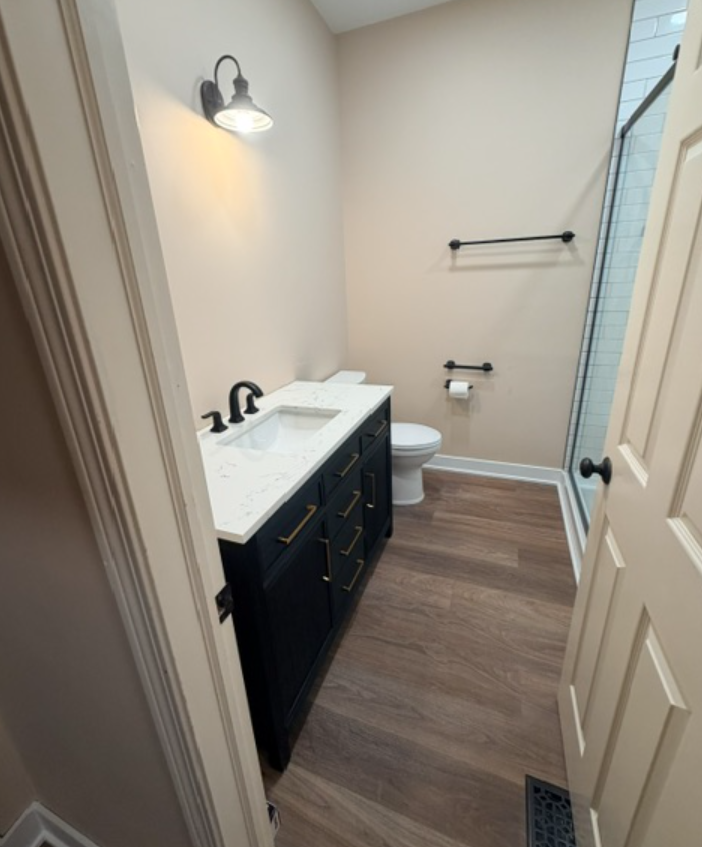 Small bathroom with dark vanity, white sink, toilet, towel bar, and shower door.