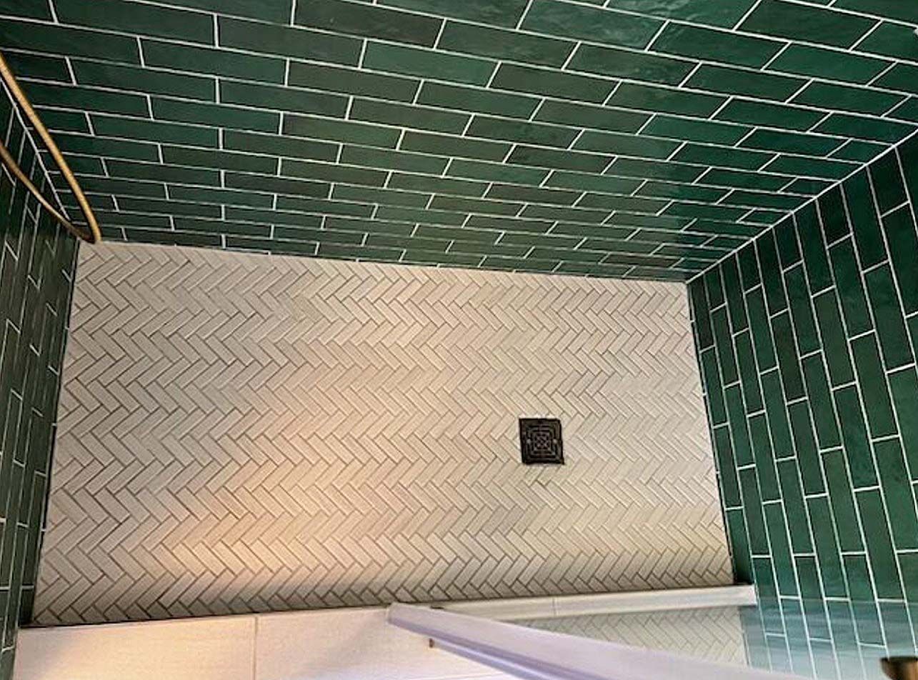 Green tiled shower interior with white herringbone wall and small black fixture.
