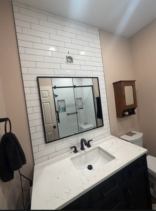 Bathroom vanity with white subway tile, black-framed mirror, sink, and wooden wall cabinet