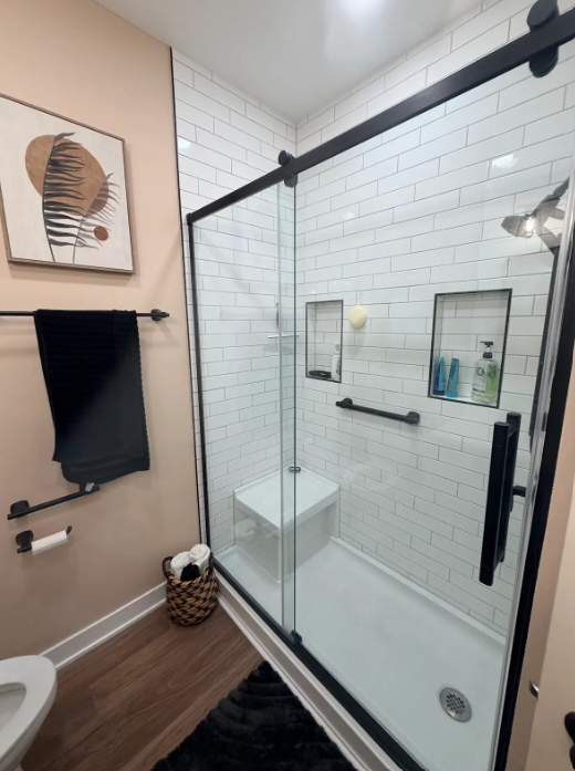 Modern bathroom with black-framed glass shower, white subway tile, and wood-look floor.