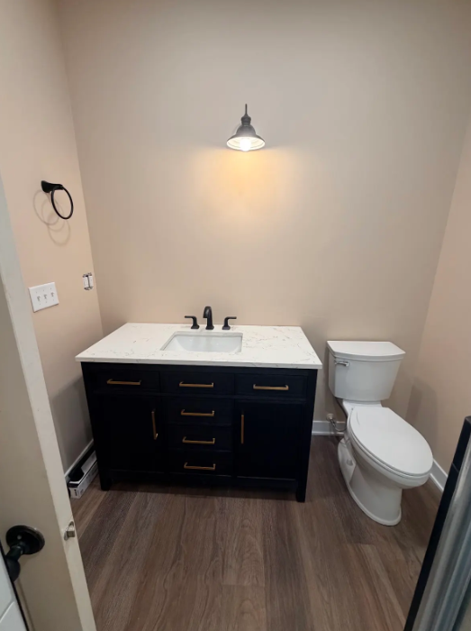 Small bathroom with dark vanity, white sink, toilet, and wall light.