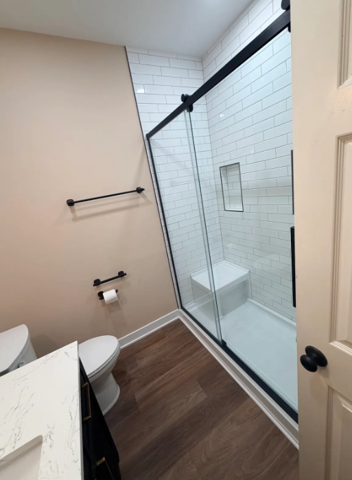 Small bathroom with a toilet, sink, and glass-enclosed shower with white tile walls.