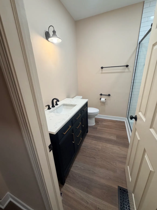 Small bathroom with dark vanity, white sink, toilet, towel rack, and glass shower door
