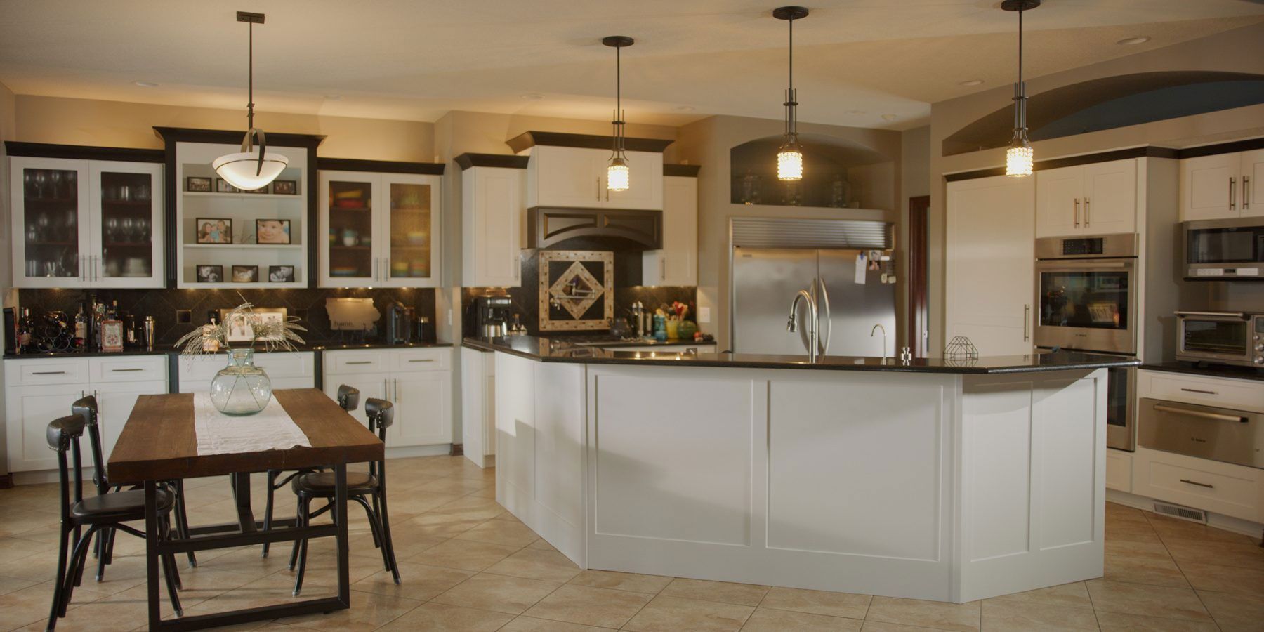 Modern open-concept kitchen with white cabinets, island, and dining table under pendant lights.