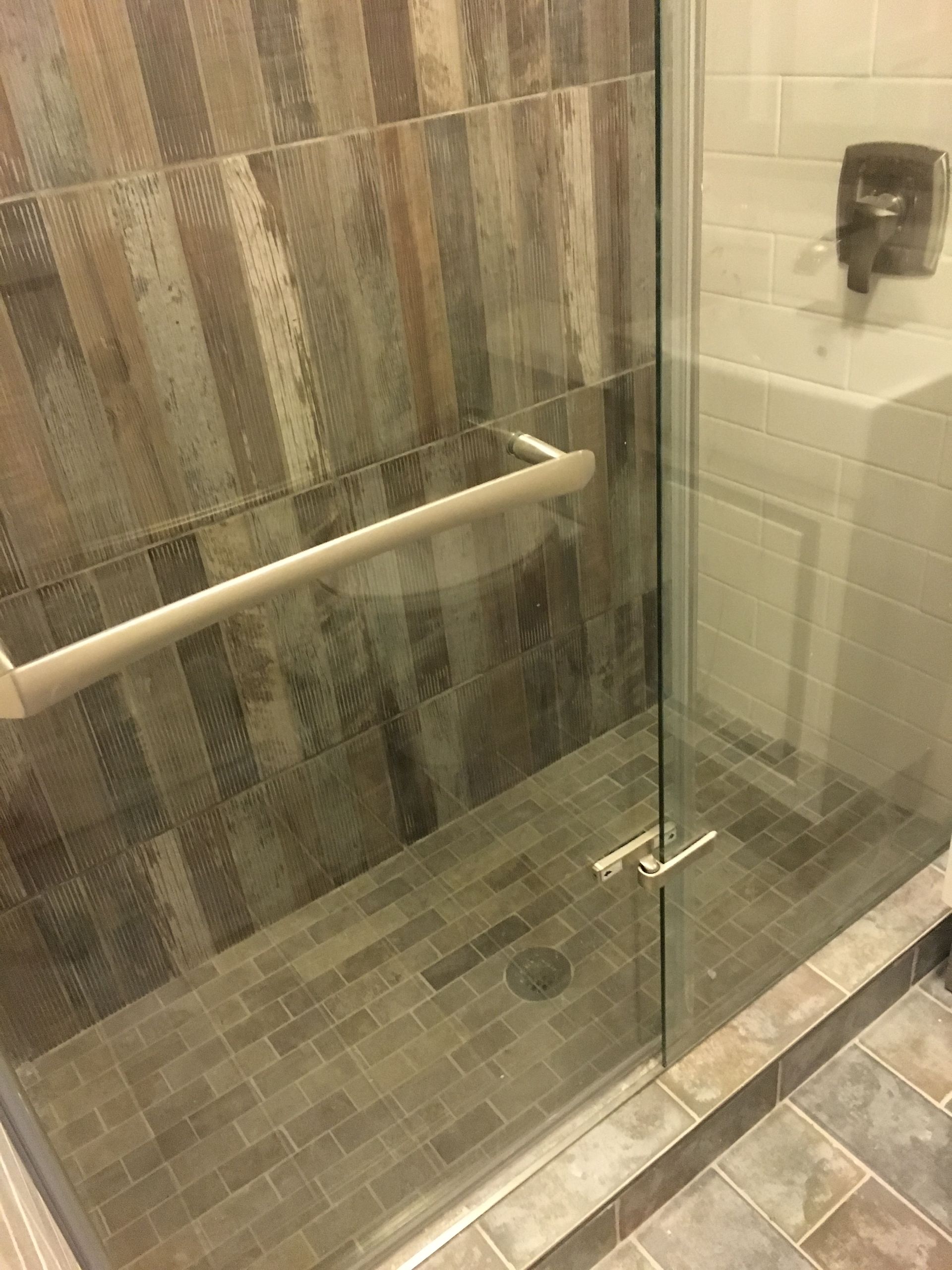 Glass shower enclosure with beige tile walls, white grab bar, and tiled floor.