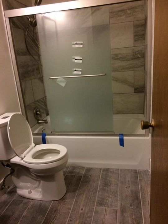 Accessible bathroom with toilet beside a frosted glass shower/tub enclosure and gray tile floor.