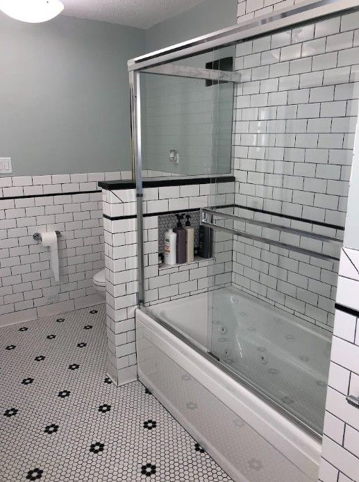 Modern bathroom with white tile, a glass-enclosed bathtub, and a showerhead on the wall.