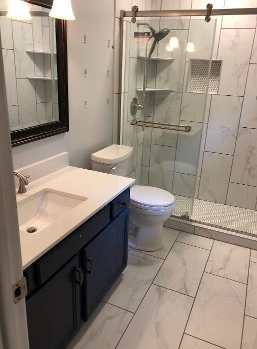 Modern bathroom with white tile, glass shower, toilet, sink, and dark vanity.