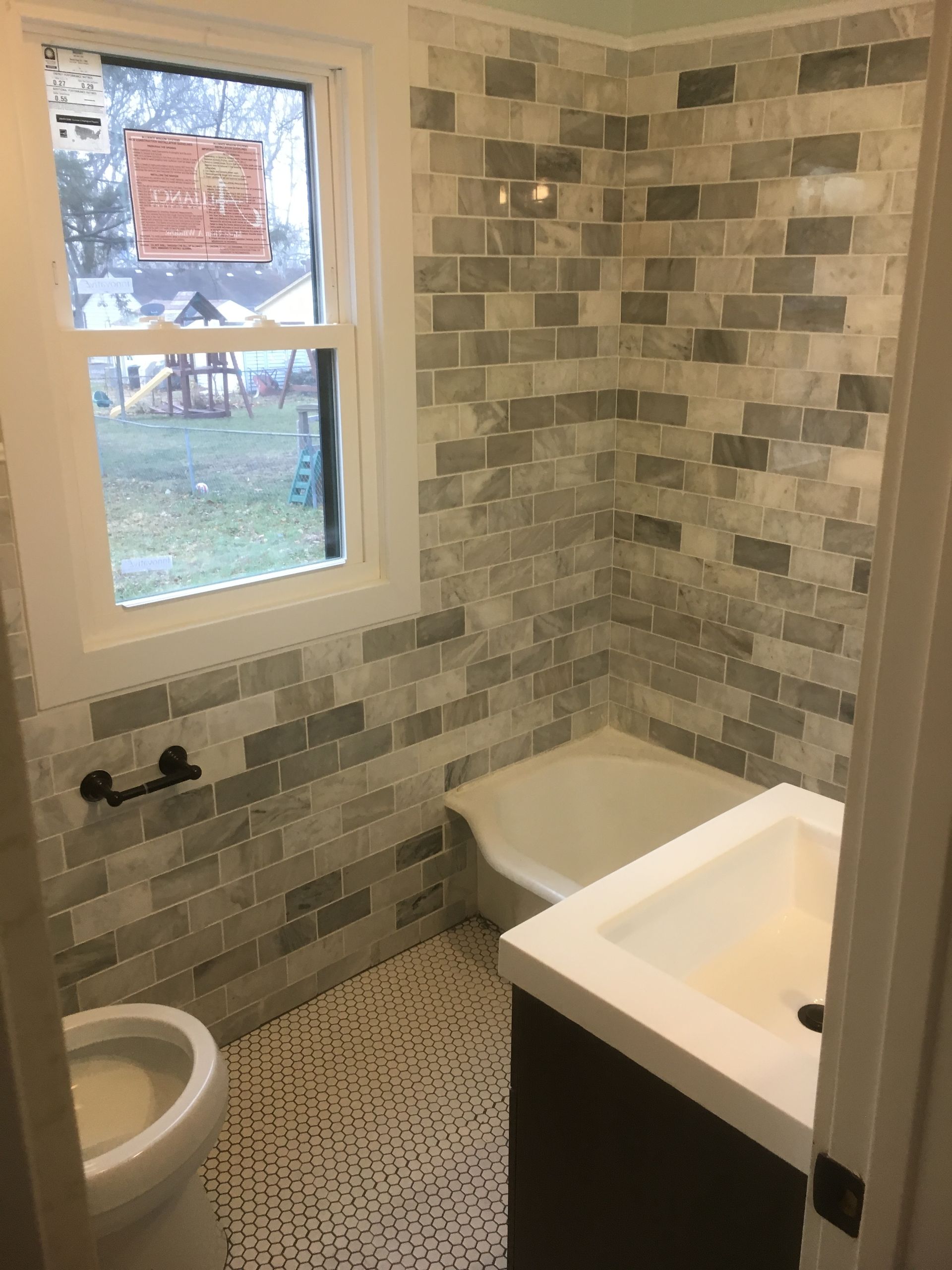 Small bathroom with tiled walls, a window, toilet, and white sink vanity.