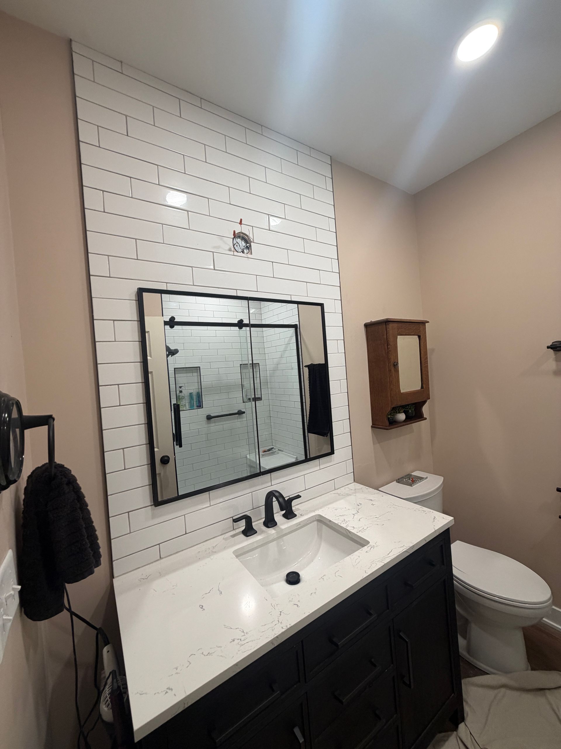 Modern bathroom with white tiled wall, black vanity, mirror, sink, toilet, and shower curtain.