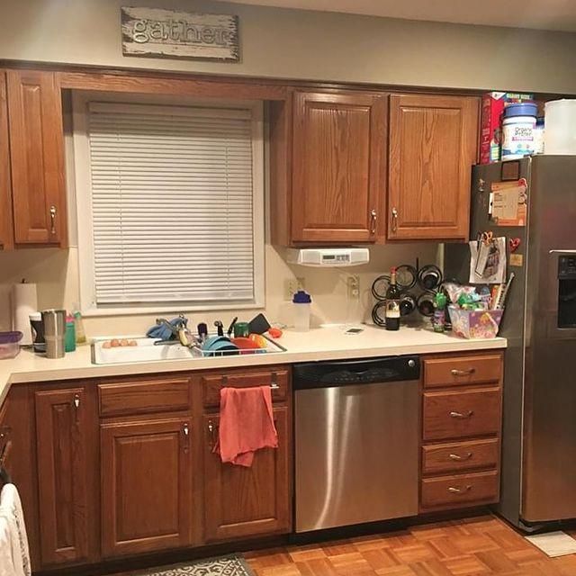 Kitchen with wooden cabinets, stainless steel dishwasher and fridge, cluttered countertop, and window blinds.